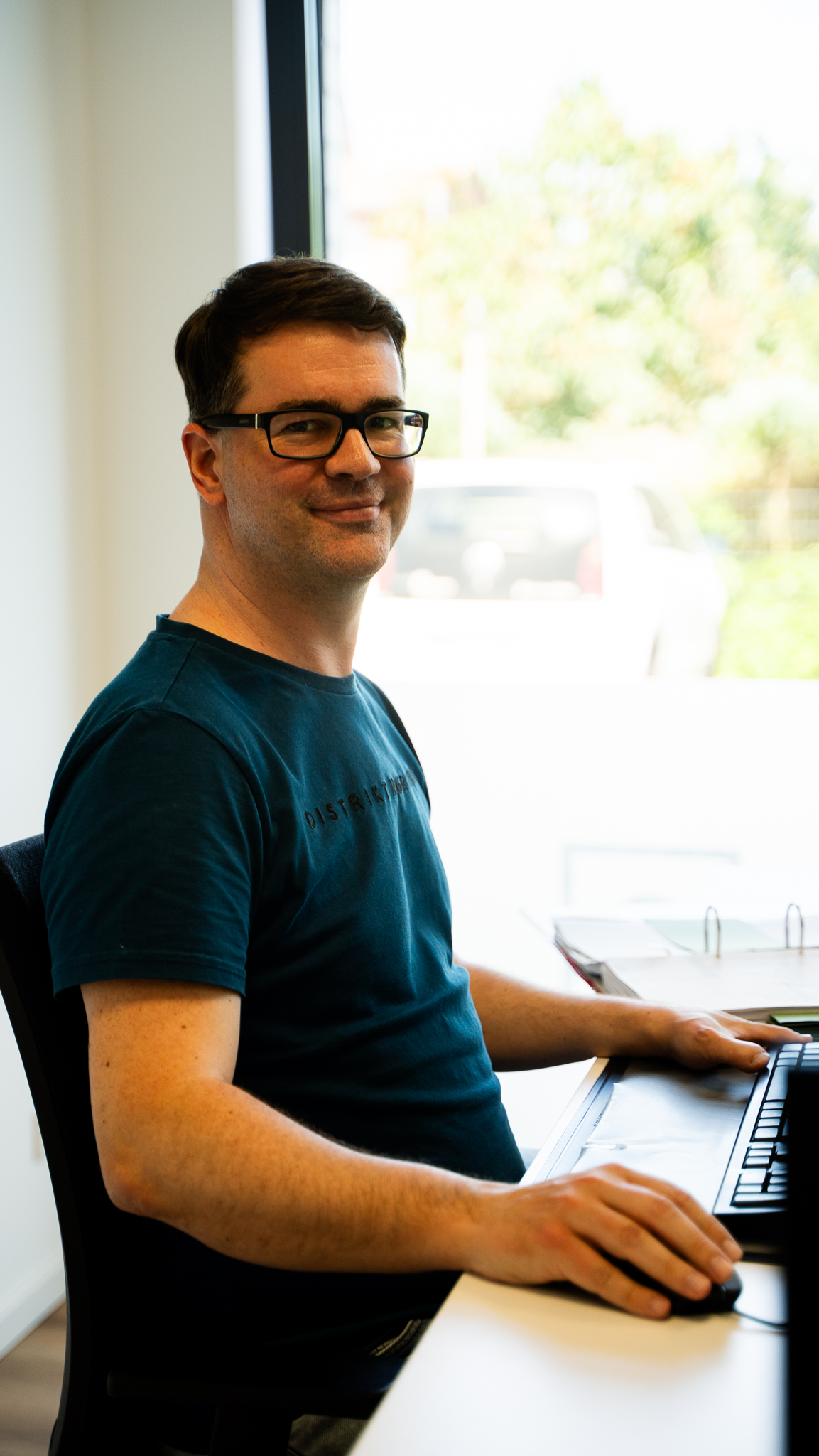 Mitarbeiter schaut an seinem Arbeitsplatz in die Kamera.