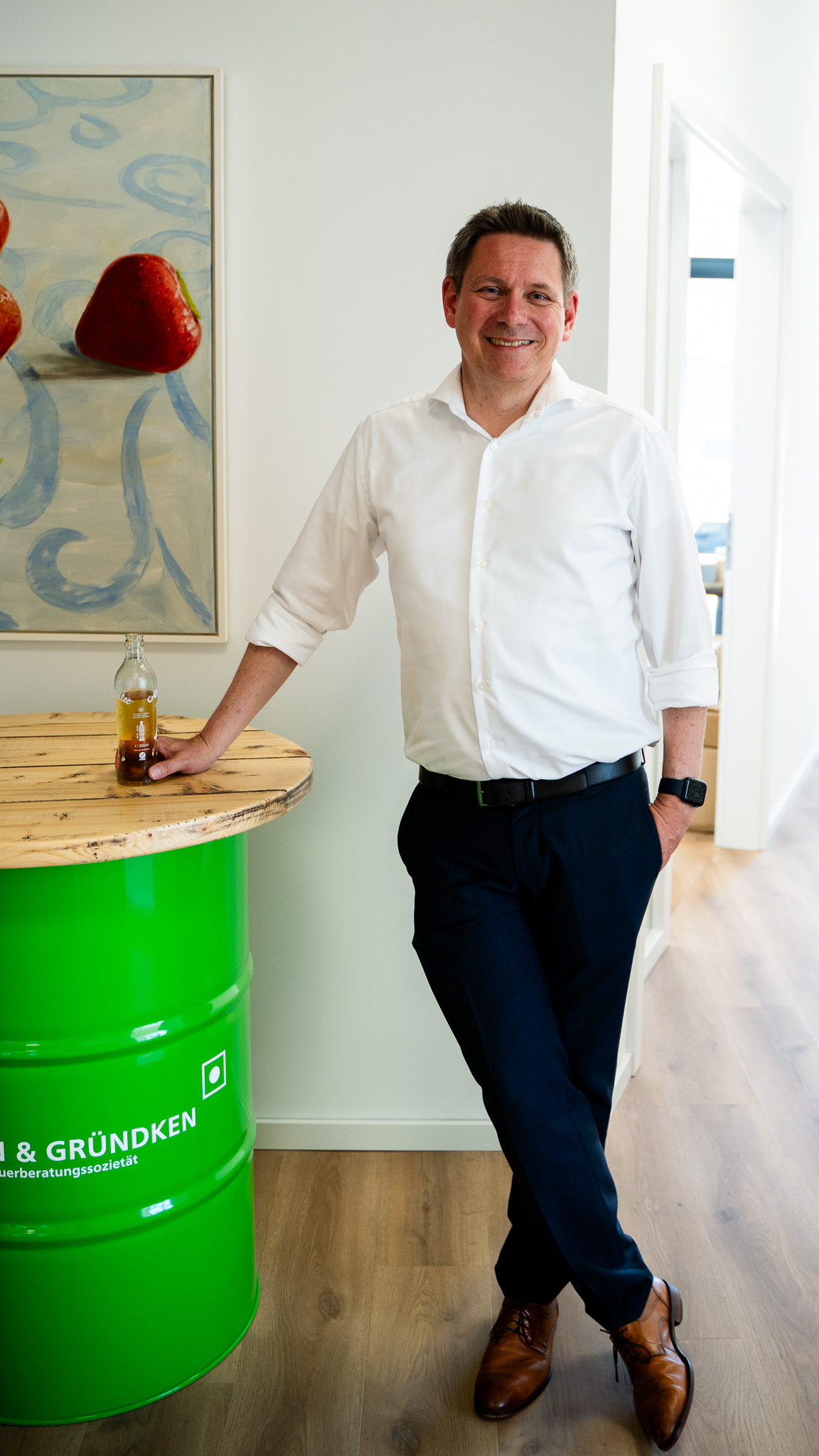 Maennliche Person lehnt an einem runden Tisch und schaut freundlich in die Kamera.